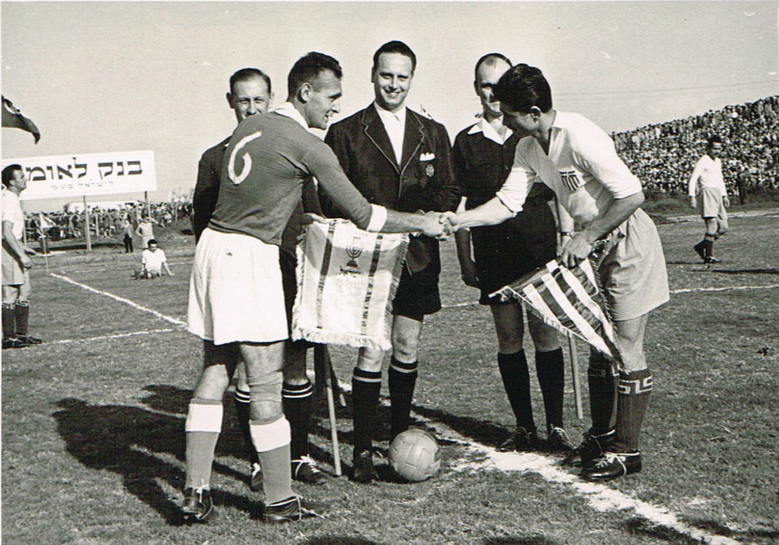קפטן נבחרת ישראל, אלי פוקס, מחליף דגלים עם הקפטן הייווני לפני המשחק ב-1954 באצטדיון רמת גן